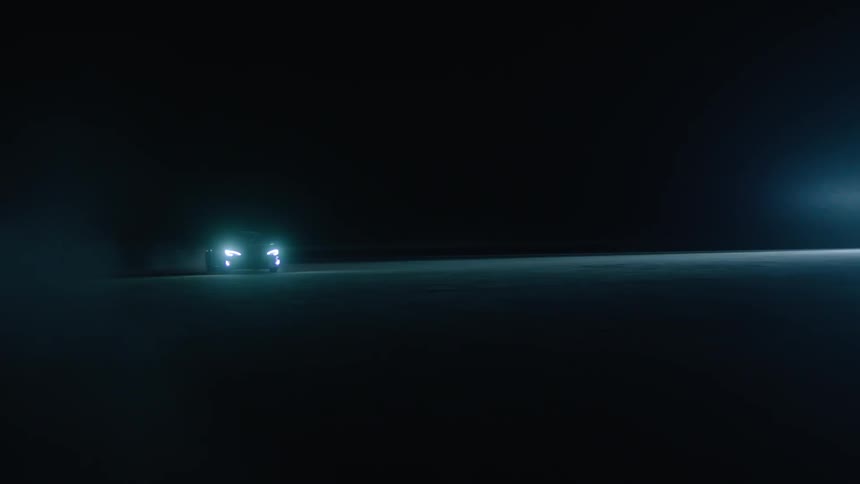 A car drives with its headlights on at night