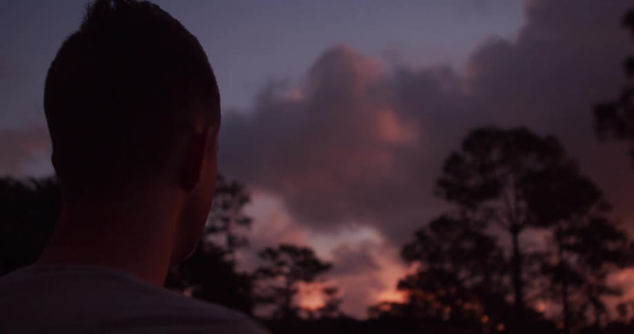 Man watches sunset in wooded area with colorful sky in the background