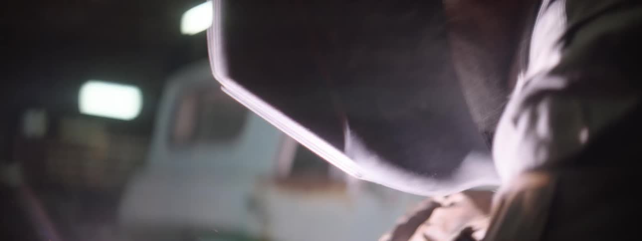 Sparks fly around a welder in a mask