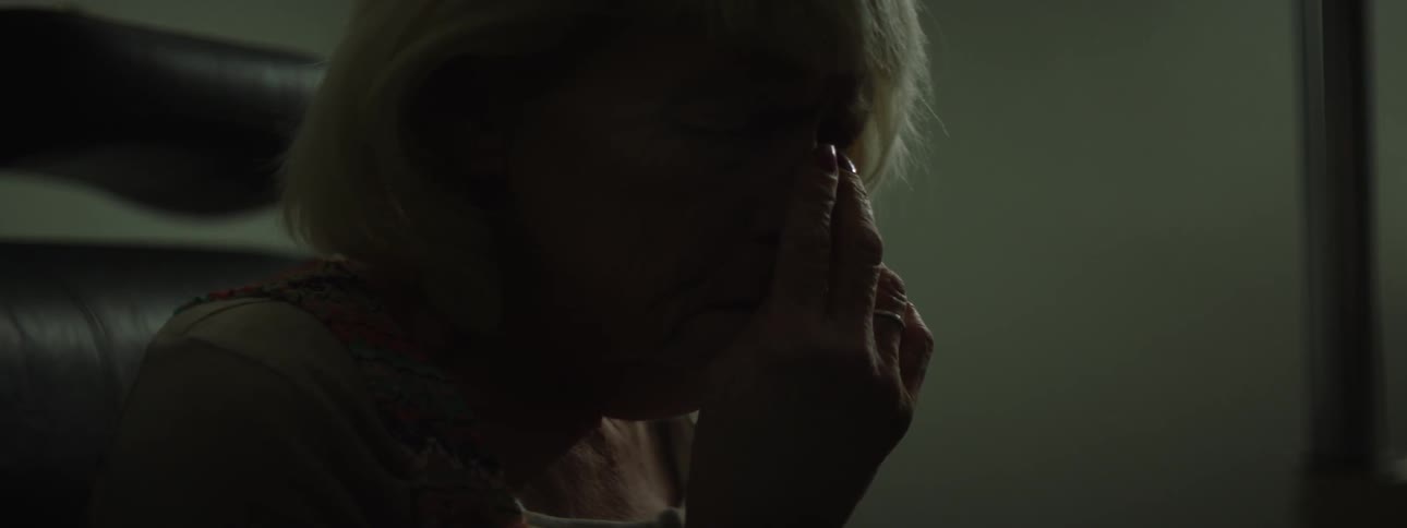 An elderly woman sits with her hand on her face