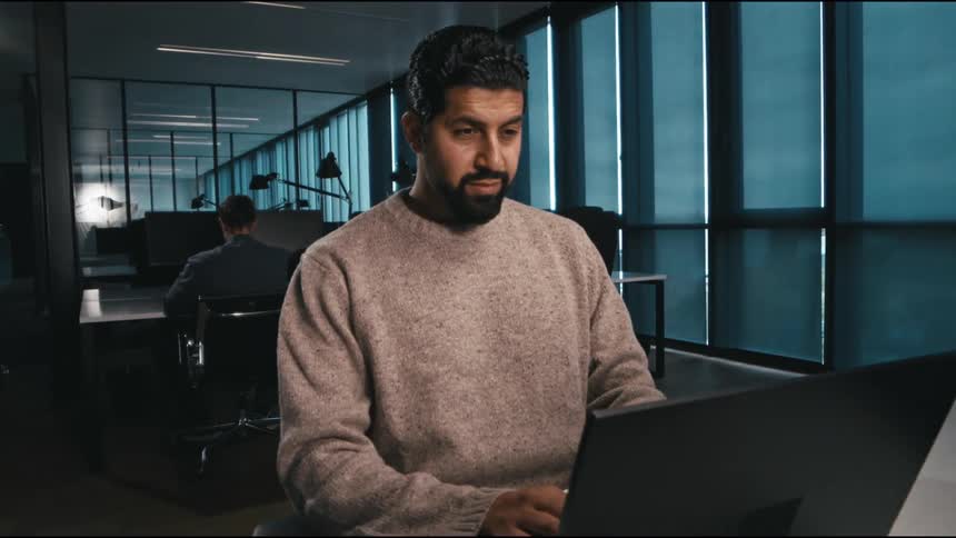 a man typing while using a laptop at a desk in a workplace