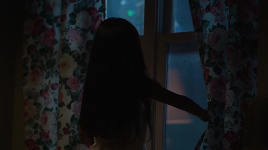 A little girl with long hair looks out of a window