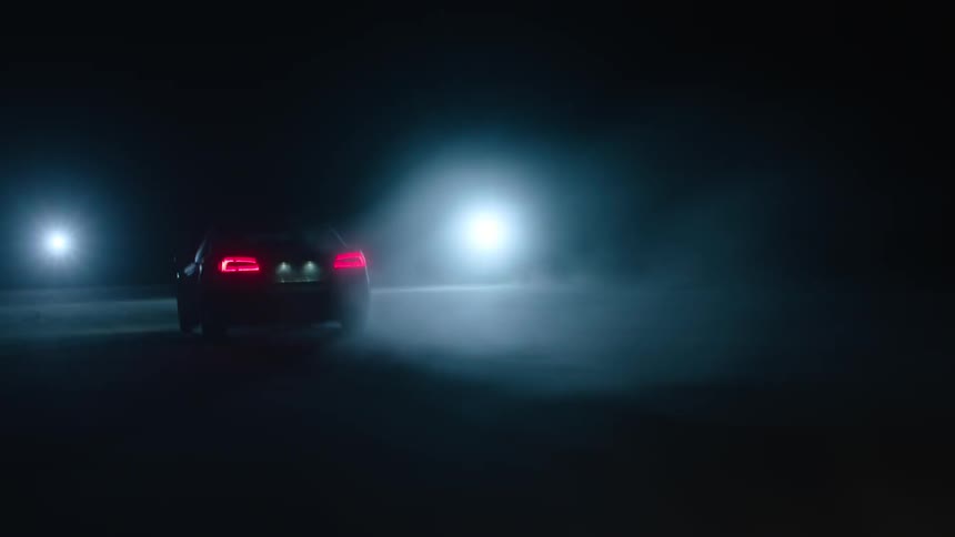 Car driving on pavement at night towards two bright lights