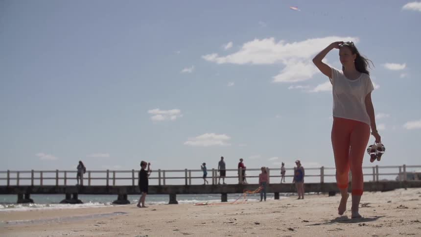 Woman walking down a beach as others stand around behind her