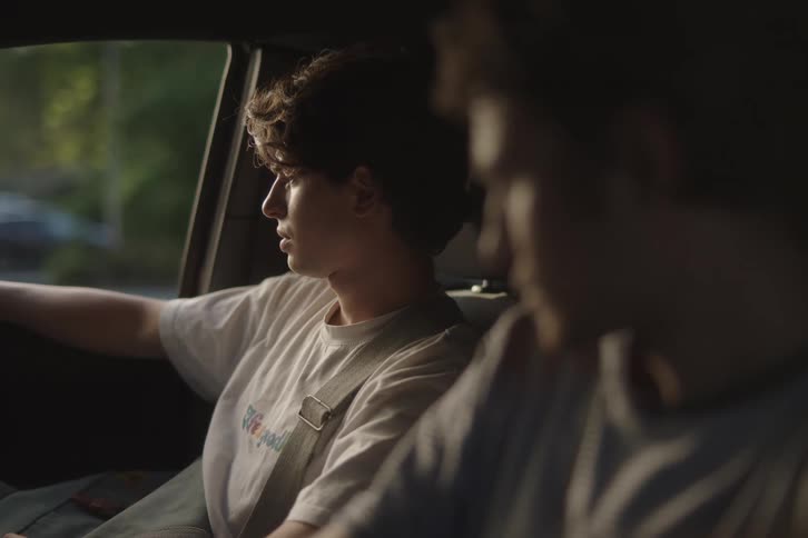Young man drives a car while talking to the passenger beside him