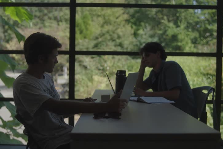 Two men studying in front of large windows overlooking trees