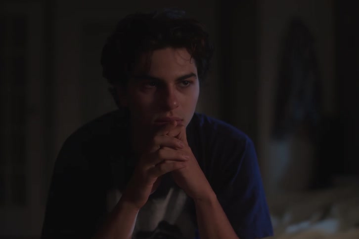 A male teen contemplating while sitting in bed in a room at night
