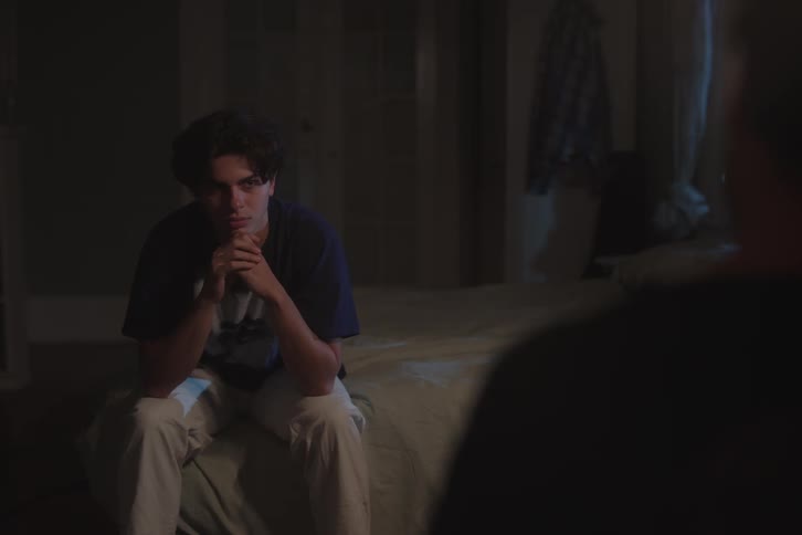 The teenager is talking while sitting on the bed