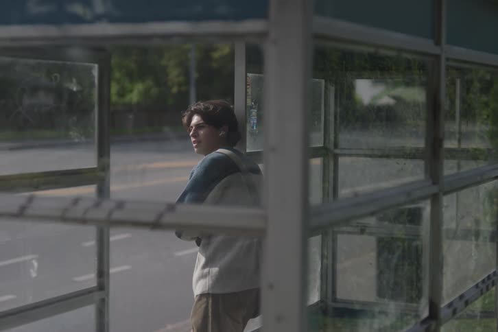 The teenager is waiting at the bus stop