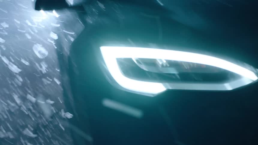 A car headlight jiggles with a lot of white debris floating in the air