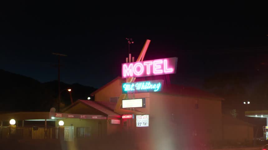 A bus drives by a motel with a lit sign at night