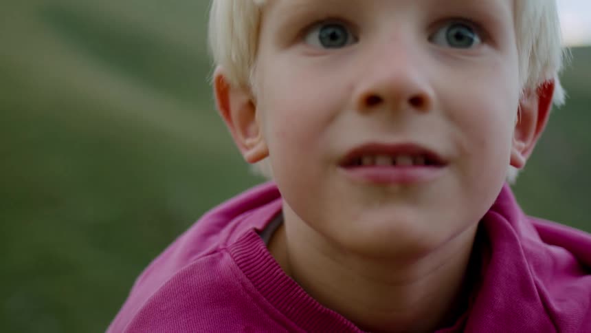 A child with blond hair smiles while outside