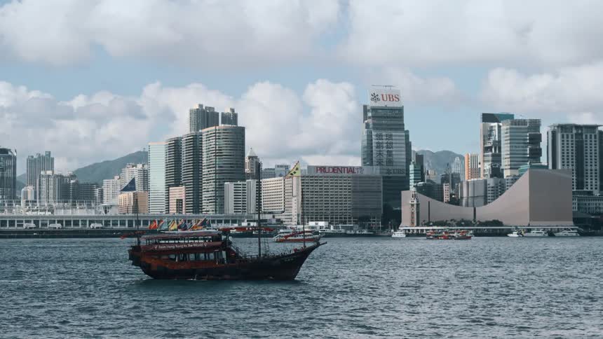 Traditional boat sailing in the harbor with modern skyscrapers in the background