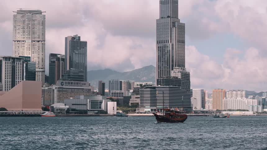 Traditional boat sails in front of modern skyscrapers by the waterfront