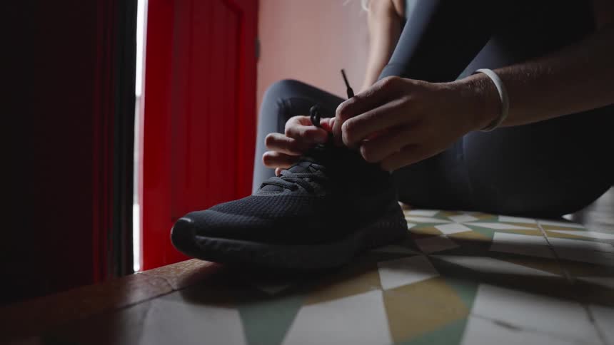 Person tying a sneaker lace near a red door