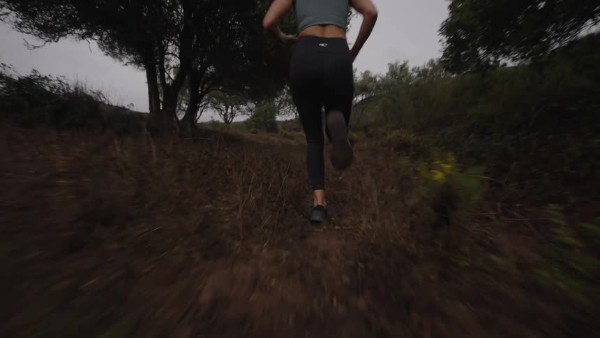 Woman running along a dirt trail surrounded by trees and low vegetation