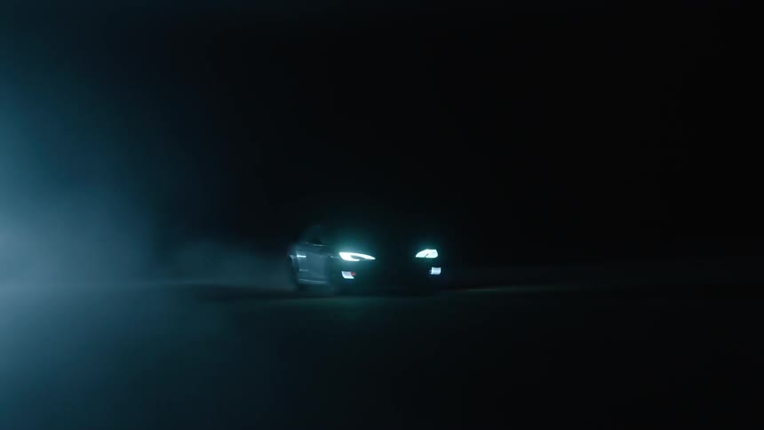 A car drives with its headlights on at night