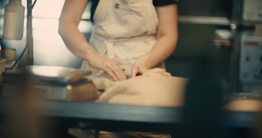 Person wearing an apron shaping bread doughs on a bakery counter