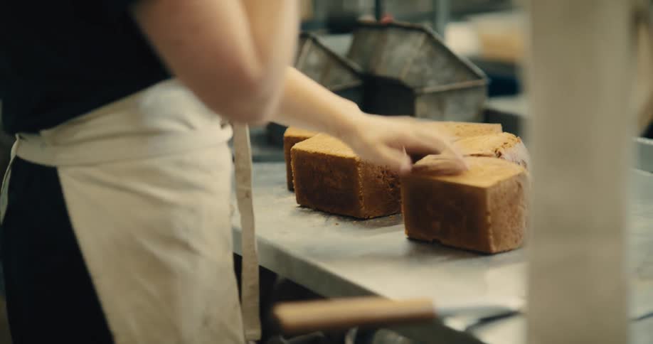 A medium close up of a baker tapping freshly baked loaves of bread checking for consistency