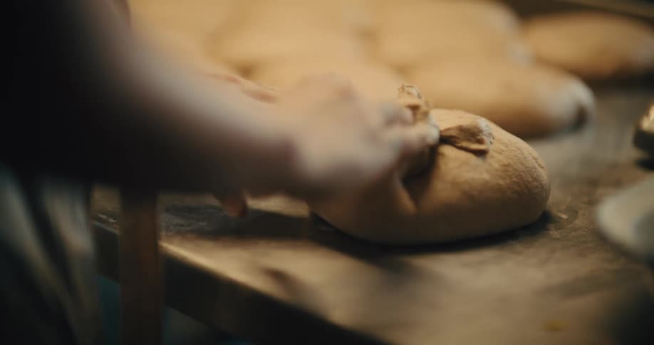A persons hands rapidly folding and shaping a lightbrown mound of dough on a dark flourdusted countertop