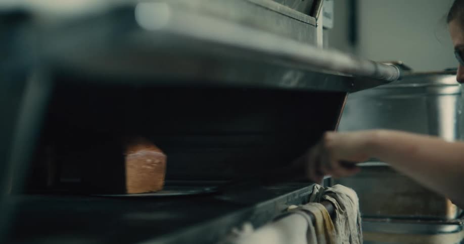 Close up of a young woman removing baked bread from an oven in a bakery during daytime