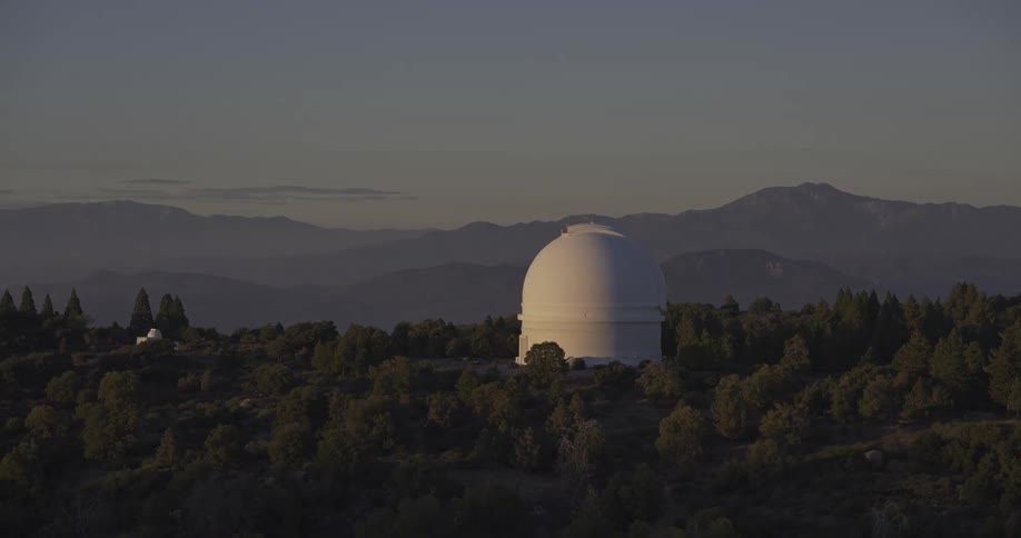White dome observatory surrounded by trees and mountains at sunset