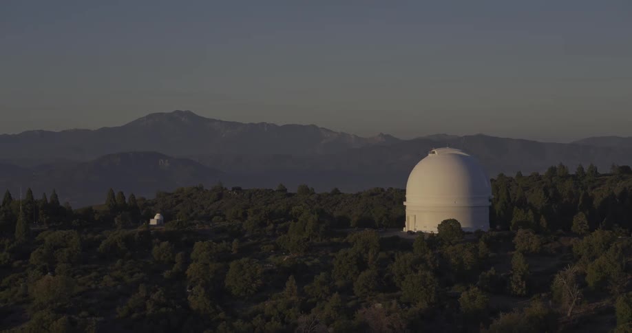 White observatory surrounded by trees with a mountain range on the background outdoors during dusk or dawn
