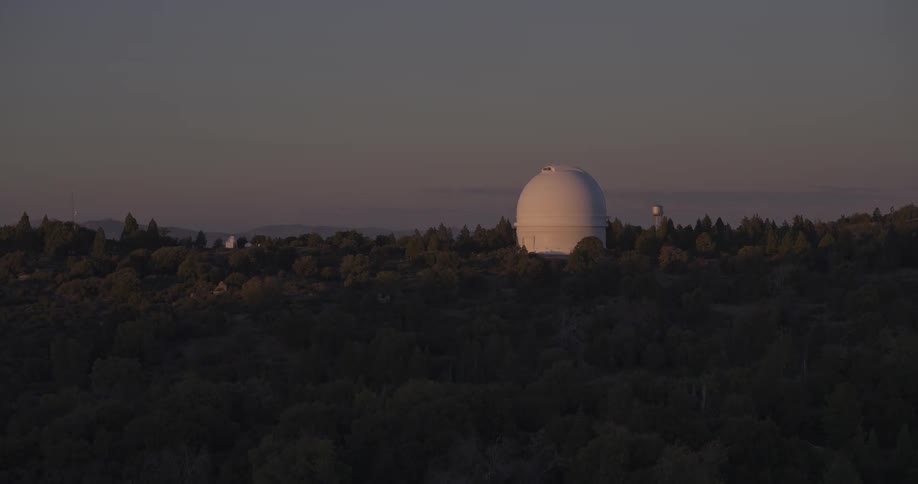 White observatory among trees under the pinkish sunset sky
