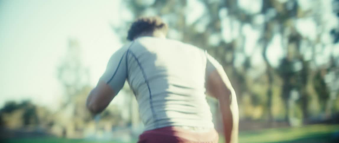 An athlete runs across a sunlit grassy field in a park