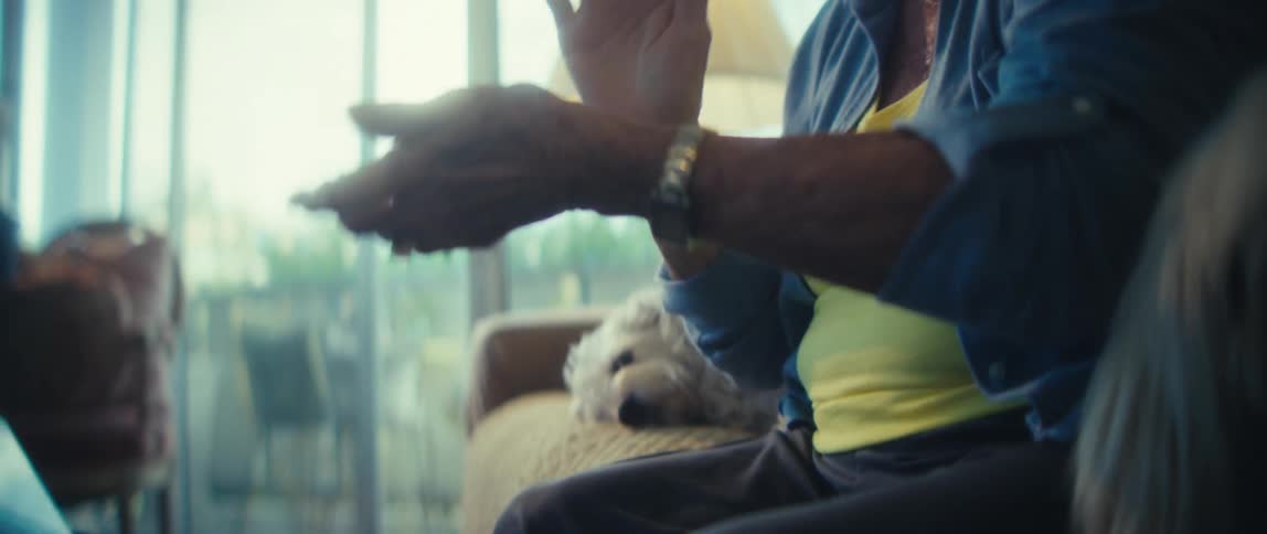 A joyful elderly woman claps her hands enthusiastically while sitting indoors with her two dogs