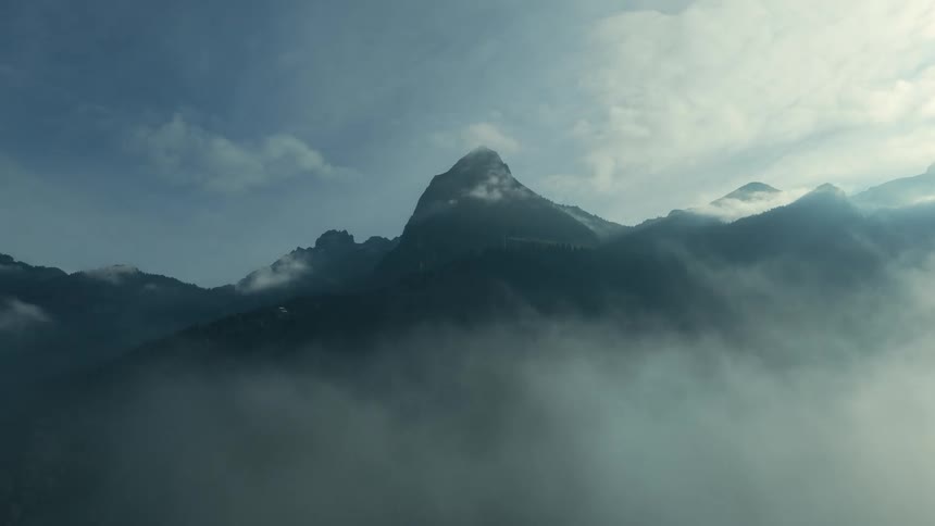 Low lying clouds partially obscure the mountains in a mountain range during the daytime