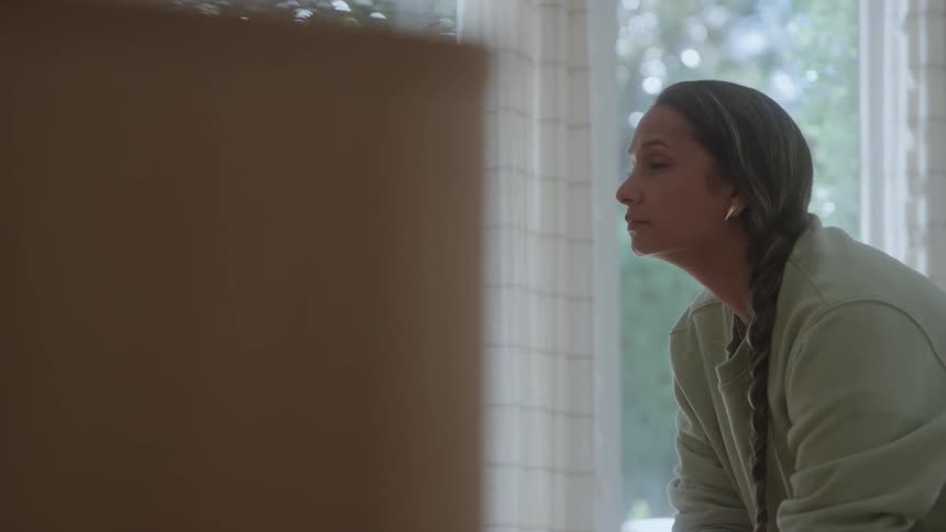 The woman is sitting and leaning forward at home