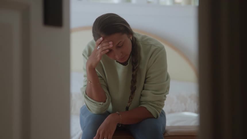 The woman looks depressed while sitting on her bed