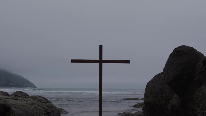A religious cross stands on a beach while ocean waves roll into the shore