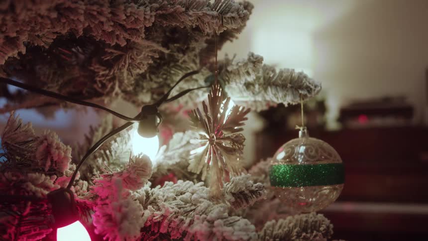 A person adjusts a delicate snowflake ornament hanging on a frosted christmas tree
