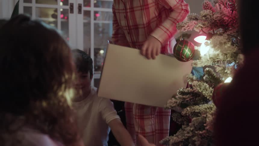A man watches his children open presents while sitting around a christmas tree