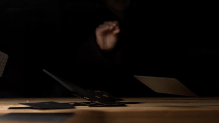 Playing cards being tossed onto a wooden table in a dark setting