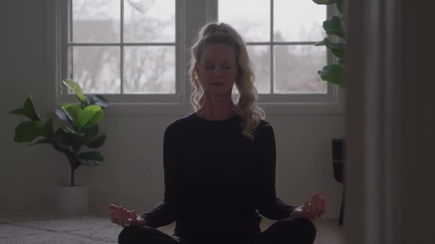 Woman sitting on the floor in a meditation pose in front of a bright window