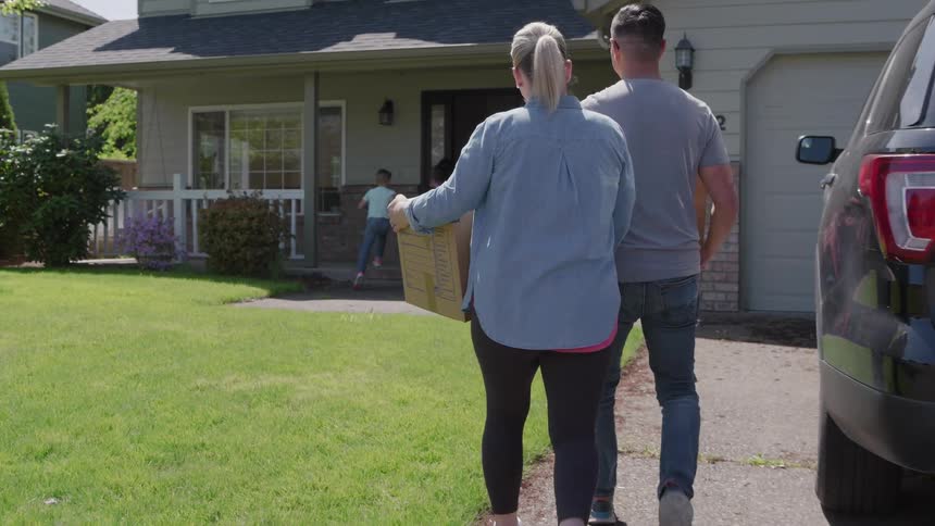 The parents follow the children into the home while carrying boxes