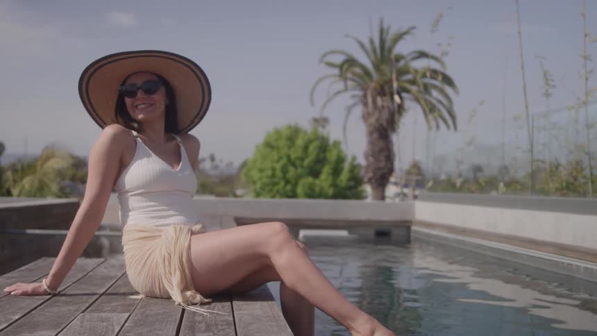 Woman relaxing by the pool wearing a widebrimmed hat and a light skirt on a sunny day