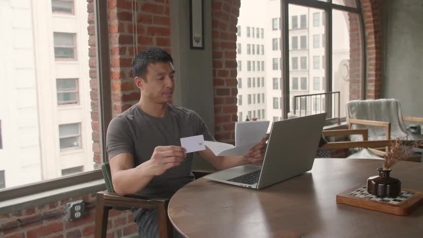 Man consults paperwork while working on his computer at home