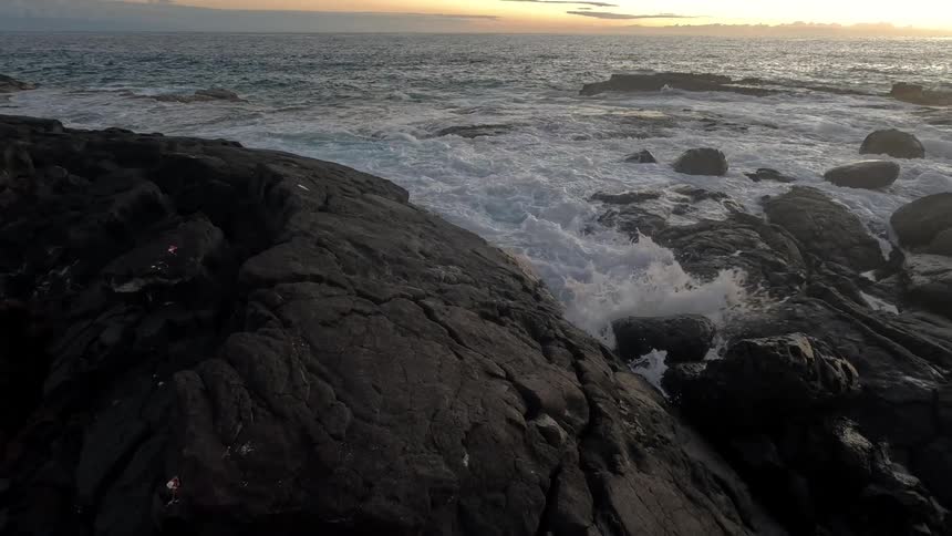 Waves foam while crashing against the rocks on the coast at sunrise