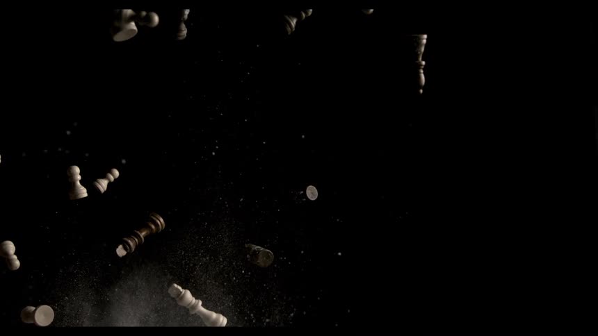 A dynamic slowmotion shot shows white and dark wooden chess pieces exploding upwards from the bottom of the frame against a solid black background