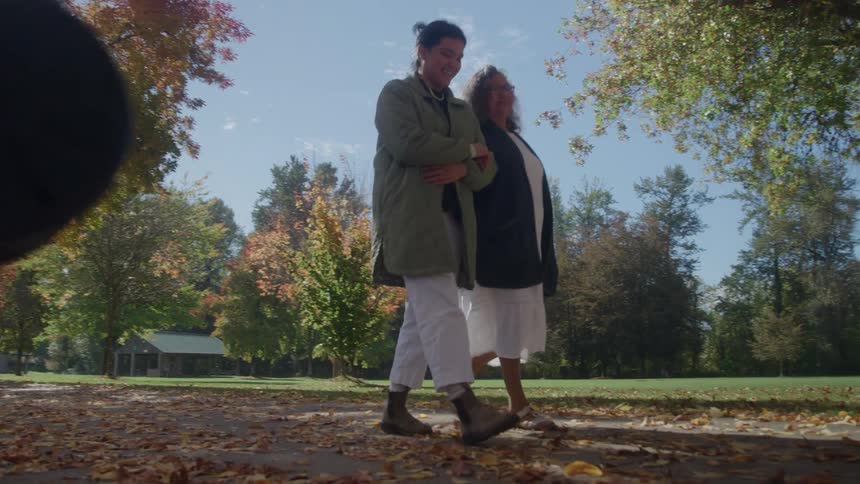 Two women walking side by side in a park surrounded by autumncolored trees