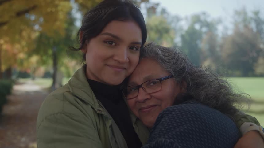 A young woman warmly embraces an older woman in a park during autumn