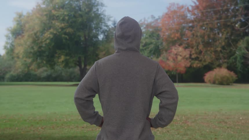 Person wearing a hoodie stands in a park looking around on an autumn day