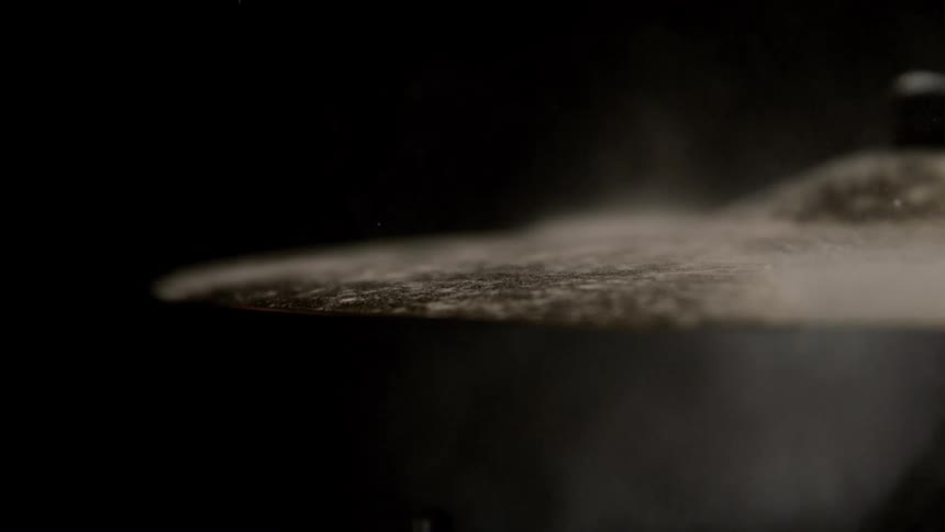 Drumstick striking a cymbal with dust particles dispersing in the air