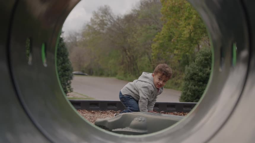 Seen from inside a playground tube a young boy on his knees looks back and smiles