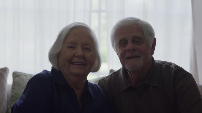 Elderly couple smiles while posing together on their couch