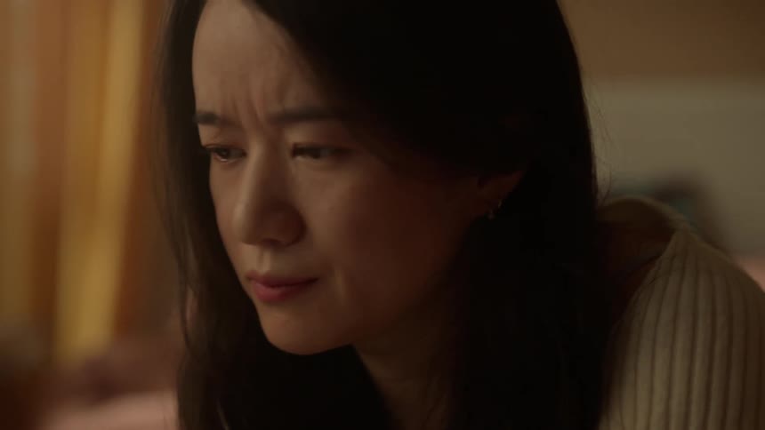 A young asian woman is browsing at a laptop then looks at the screen with a focused expression that ends with a slight upward turn of the mouth in a bedroom setting